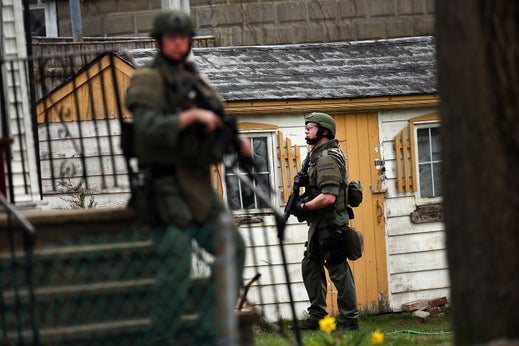 Members of a police S.W.A.T. team search through a neighborhood in Watertown
